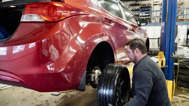 Un garagiste de Trois-Rivières installe des pneus d'hiver sur une voiture rouge.