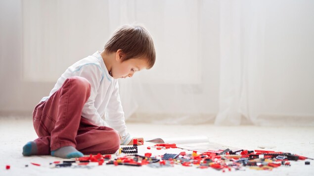 Un enfant est assis par terre. Autour de lui, des blocs de constructions rouges, noirs et gris sont près de lui. Un enfant est assis par terre. Autour de lui, des blocs de constructions rouges, noirs et gris sont près de lui.