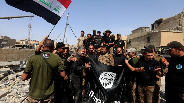 Des membres des forces irakiennes de contre-terrorisme brandissent un drapeau de l'État islamique. Des membres des forces irakiennes de contre-terrorisme brandissent un drapeau de l'État islamique.