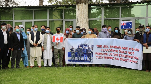 Des interprètes afghans, qui sont debout côte à côte, tiennent une banderole qui dénonce les talibans.
