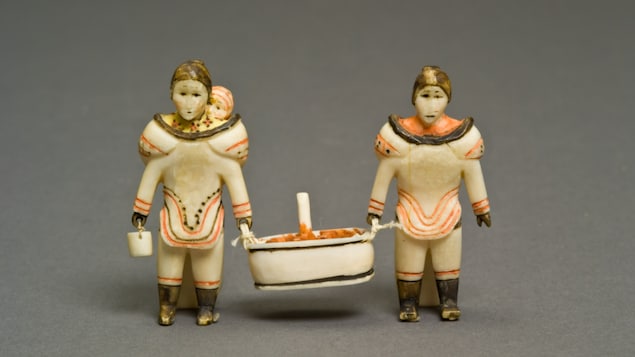 An ivory carving of two women carrying a basket. 