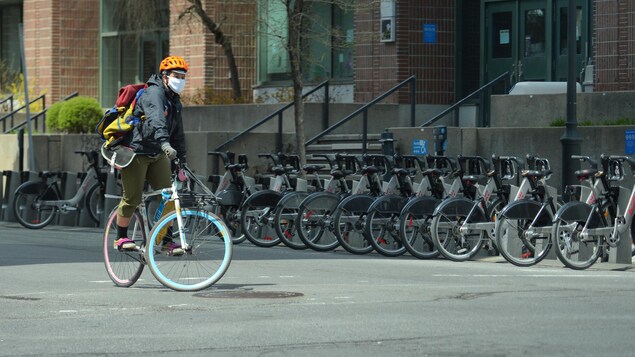 Un cycliste portant un masque roule devant une station de vélos BIXI.