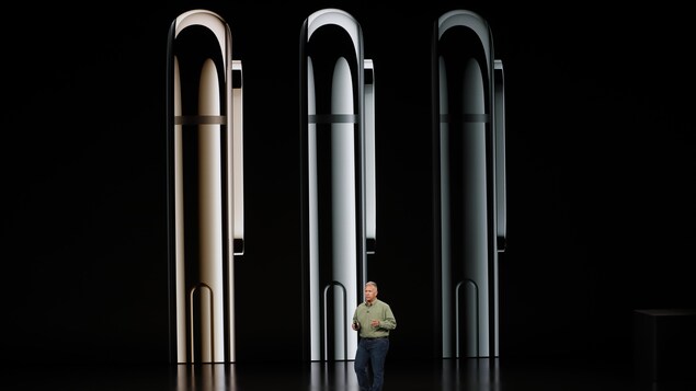 Une photo montrant le profil de trois iPhone X S en différentes couleurs. Un homme est debout devant le grand écran. Une photo montrant le profil de trois iPhone X S en différentes couleurs. Un homme est debout devant le grand écran.