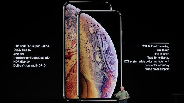 Une photo montrant un iPhone X S et un iPhone X S Max sur un écran géant. Un homme se tient debout devant l'écran. Une photo montrant un iPhone X S et un iPhone X S Max sur un écran géant. Un homme se tient debout devant l'écran.