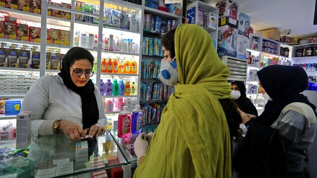 Des clientes portant un masque sont au comptoir d'une pharmacie.