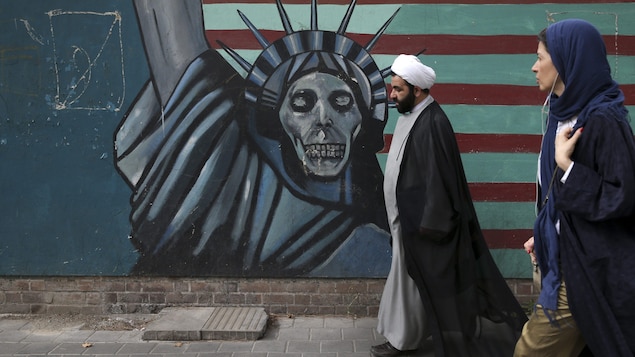 Un religieux chiite et une femme marchent devant une murale caricaturant le statue de la liberté. Le visage de la statue a été remplacé par une tête de mort. . Un religieux chiite et une femme marchent devant une murale caricaturant le statue de la liberté. Le visage de la statue a été remplacé par une tête de mort. .