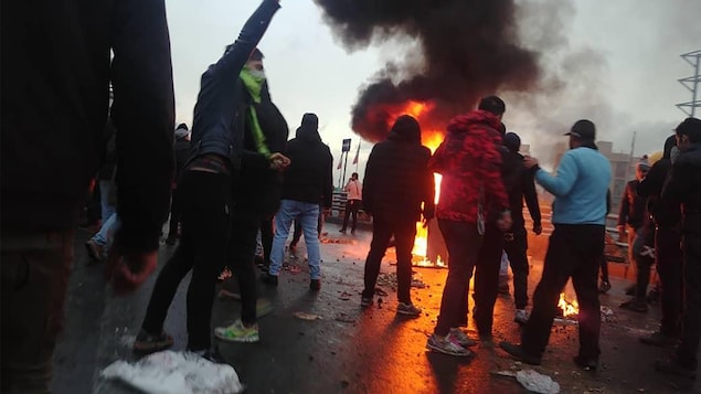 Des protestataires sont rassemblés près d'un brasier, dans la rue.