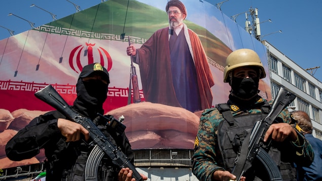 Des hommes lourdement armés sous un grand portrait du nouveau guide suprême iranien, Mojtaba Khamenei.