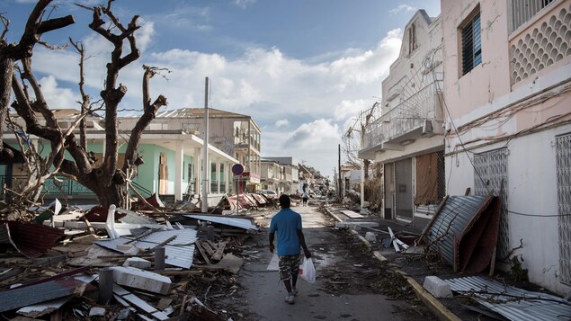 Un homme marche dans une rue bordée de débris et de bâtiments endommagés, dans la partie française de l'île de Saint-Martin.