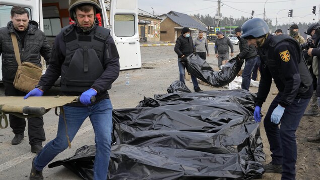 Des hommes transportent des sacs noirs qu'ils réunissent le long d'une route.