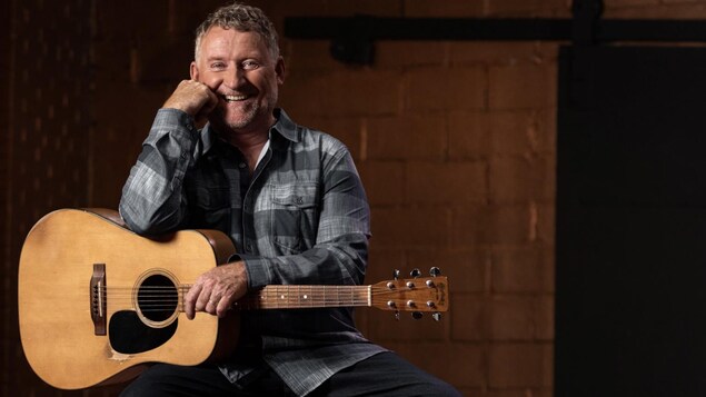 L'artiste souriant, pose avec sa guitare.