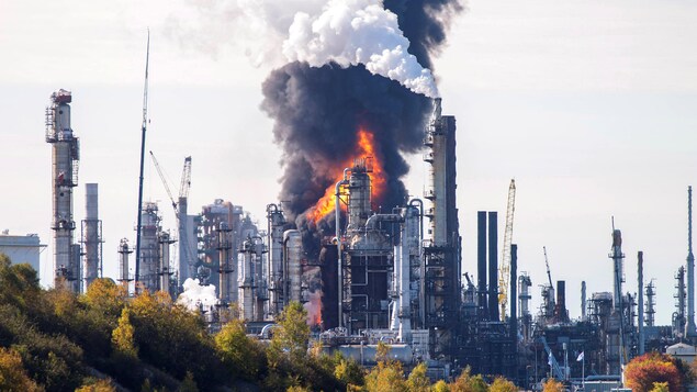 Un incendie est vu au loin, derrière des bâtiments et une colonne de fumée noire s'élève dans le ciel.
