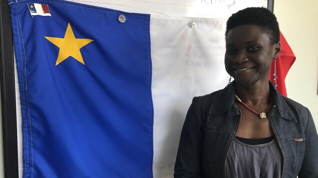 Isabelle Dasylva-Gill pose pour la photo. Un drapeau acadien se trouve derrière elle.