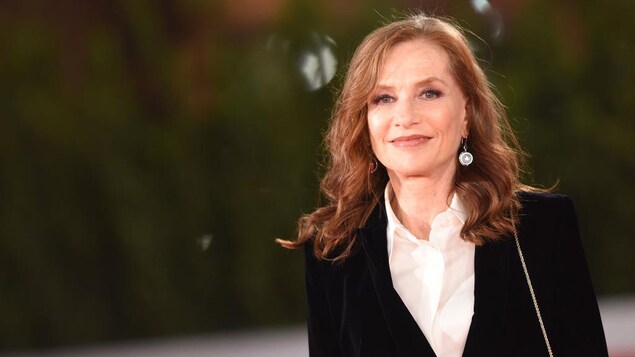 Isabelle Huppert porte une veste noire et une chemise blanche.