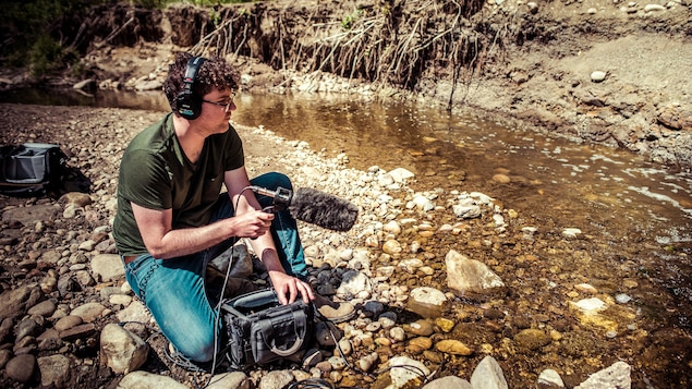 Isaël Huard assis au bord d'un cours d'eau dont il capte le bruit.