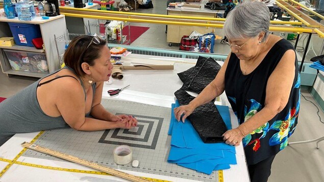 Two women look at cloth on a sewing mat. 