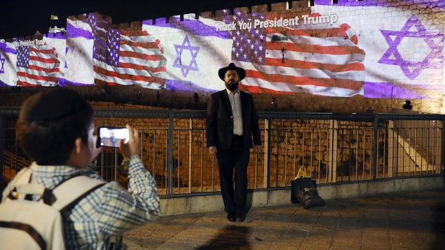 Un garçon prend une photo d'un homme habillé de façon juive traditionnelle qui se tient devant les projections.