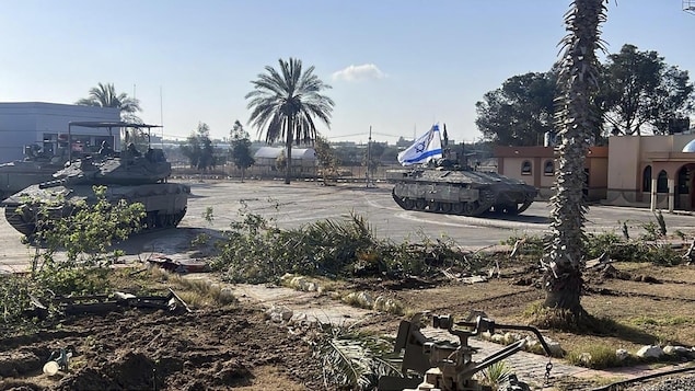 Un blindé arborant le drapeau israélien au point de passage de Rafah à côté de palmiers d'immeubles.