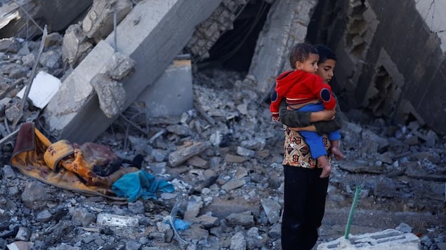 A Palestinian boy carrying a baby stands at a site of Israeli strikes, in the Rafah district of Gaza on Monday. 