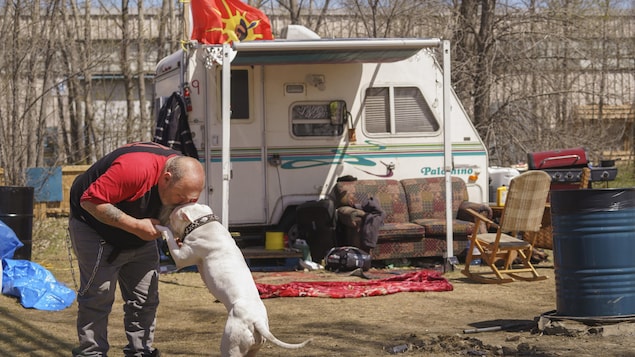Guylain Levasseur fait un câlin à son chien devant sa petite roulotte.