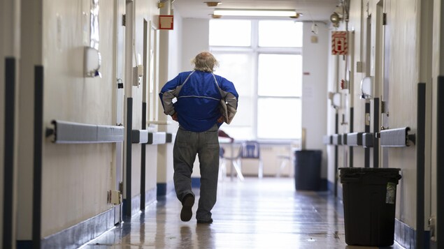 Un homme marche dans le corridor d'un hôpital en remontant son jeans.