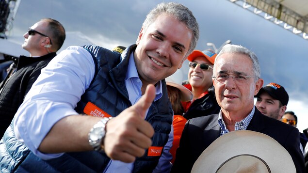 Ivan Duque, pouce en l'air et tout sourire, aux côtés d'Alvaro Uribe, qui tient son chapeau dans sa main. Ivan Duque, pouce en l'air et tout sourire, aux côtés d'Alvaro Uribe, qui tient son chapeau dans sa main.