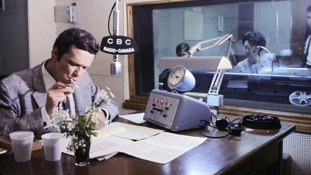 Dans un studio de radio, l'animateur Jacques Boulanger est assis à un pupitre et il révise ses notes tout en s'allumant une cigarette. Un micro est suspendu au-dessus de la table où repose un appareil de contrôle. À l'arrière-plan, on voit la réalisatrice Huguette Paré qui est derrière une vitre, dans la régie.