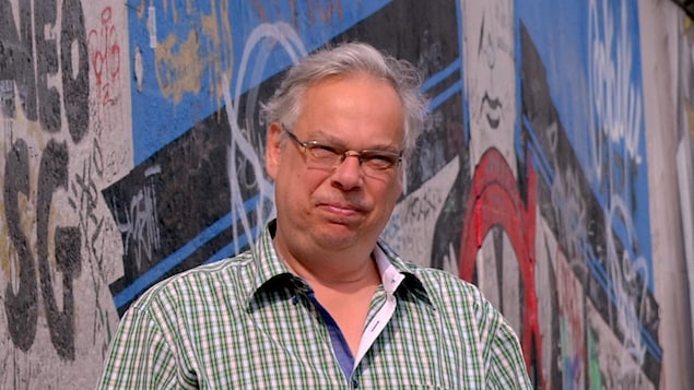 Portrait en couleur, en extérieur, de l'auteur Jacques Lemaire, devant un mur couvert de graffitis