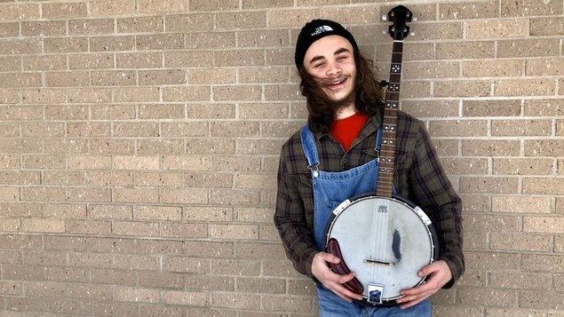 Un jeune homme en salopette souri avec son banjo dans les mains.