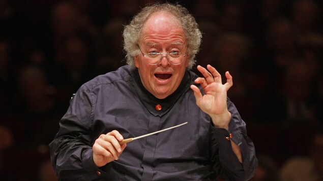 Un homme âgé dirige avec passion un orchestre devant une salle comble à New York. Un homme âgé dirige avec passion un orchestre devant une salle comble à New York.