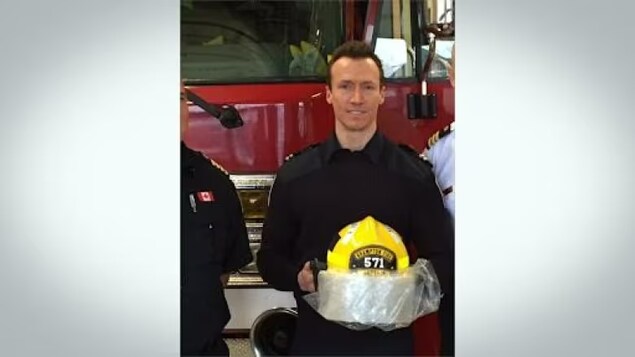L'ancien capitaine des pompiers de Brampton, James Schwalm, pose devant un camion de pompier avec son casque à la main.