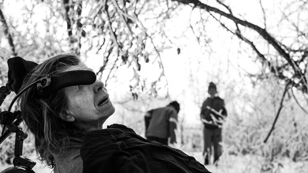 La mère de Jamie Woytiuk, est dans son fauteuil roulant. En arrière-plan, deux garçons jouent dans la neige. La mère de Jamie Woytiuk, est dans son fauteuil roulant. En arrière-plan, deux garçons jouent dans la neige.