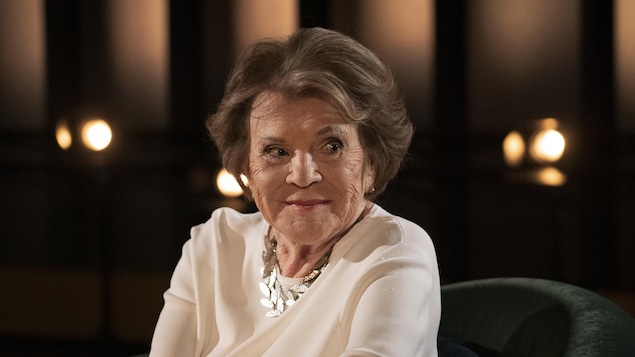 Assise, un sourire aux lèvres, Janette Bertrand regarde sur sa gauche.