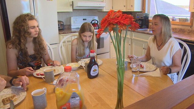 Une famille est assise à une table à manger avec des gaufres et un vase de fleurs orange. Une famille est assise à une table à manger avec des gaufres et un vase de fleurs orange.
