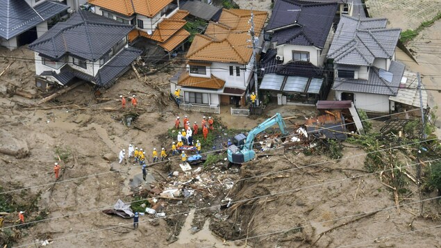 Des membres d'équipes de secours devant des débris de maisons détruites par des coulées de boue et des glissements de terrain.