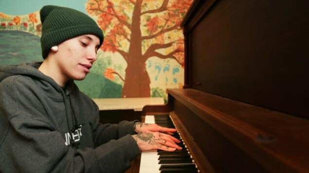 Une personne jouant du piano, une fresque peinte à la main montrant un arbre derrière elle Une personne jouant du piano, une fresque peinte à la main montrant un arbre derrière elle