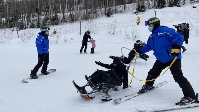 Le moniteur montre à l'enfant comment se servir de de son siège à skis.