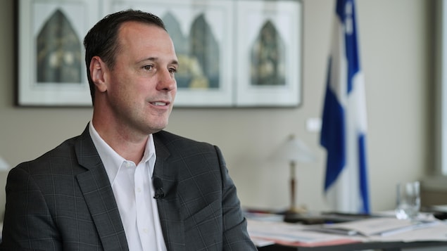 Dans son bureau, Jean-François Roberge écoute, décontracté, une question du journaliste de Radio-Canada. Des dossiers sont étalés sur son bureau derrière lui.