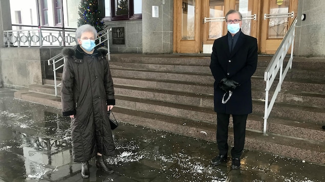 Deux personnes, une à côté de l'autre, à l'extérieur, devant l'entrée des Soeurs de la Charité