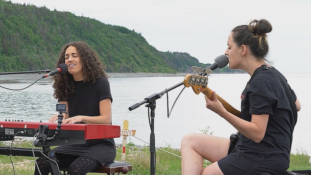 Une femme chante en jouant du clavier et un autre joue de la basse sur le bord de l'eau.
