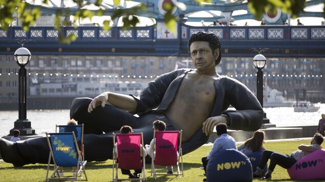 Des passants sont assis à côté de la statue géante de Jeff Goldlbum, installée à Londres. Des passants sont assis à côté de la statue géante de Jeff Goldlbum, installée à Londres.