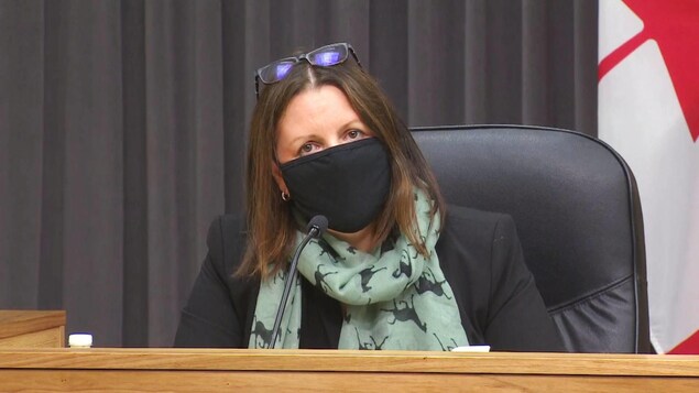 Jennifer Russell, le visage couvert d'un masque et ses lunettes sur la tête, est assise lors d'une conférence de presse.
