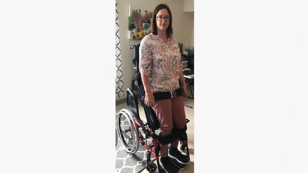 Une femme portant des lunettes se tient debout grâce à un fauteuil roulant verticalisateur. 