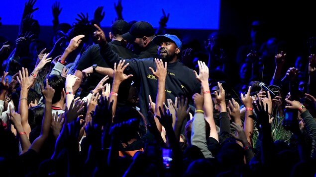 La chanteur est entouré de plusieurs personnes qui lèvent les bras.