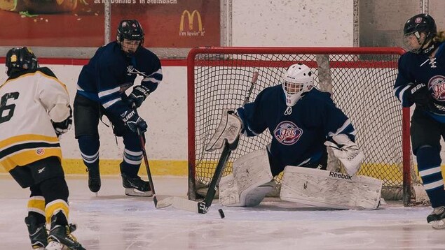 Quatre personnes jouent au hockey, le gardien bloque le but. Quatre personnes jouent au hockey, le gardien bloque le but.