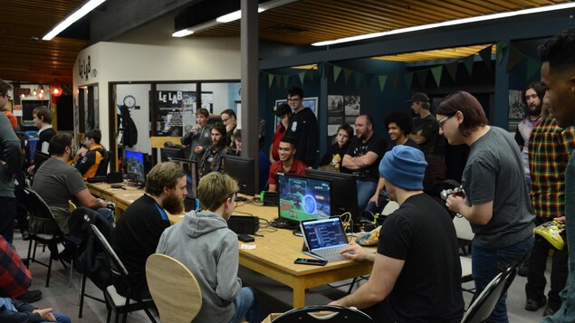Des gens sont rassemblés autour d'écrans d'ordinateurs dans une salle réservée aux jeux vidéo.