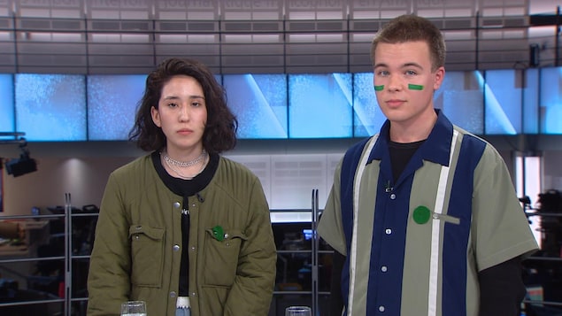 Une jeune femme et un jeune homme, tous deux portant un badge vert sur la poitrine, dans les studios de Radio-Canada à Montréal.