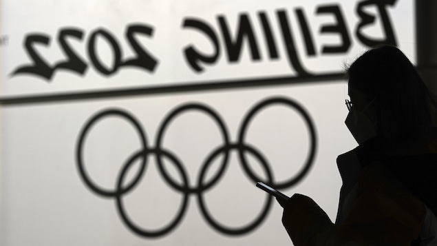 Une femme regarde son téléphone devant un logo des Jeux olympiques de Pékin.