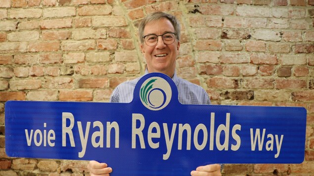 Hawak ni Jim Watson ang isang street sign na nagsasabing Ryan Reynolds Way.