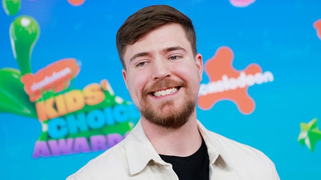 Un homme souriant devant une affiche de Nickelodeon. 